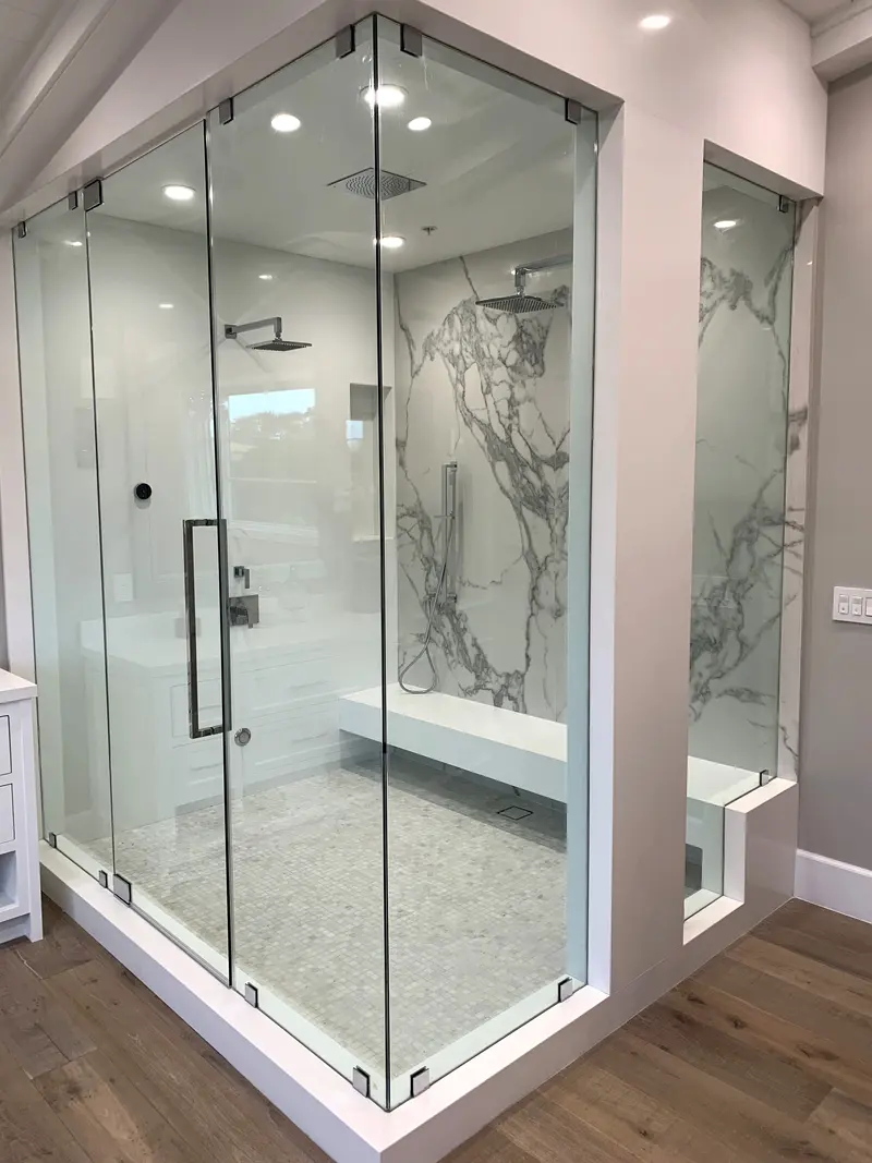 Frameless glass shower with marble slab walls and a built-in bench in a completed primary bathroom